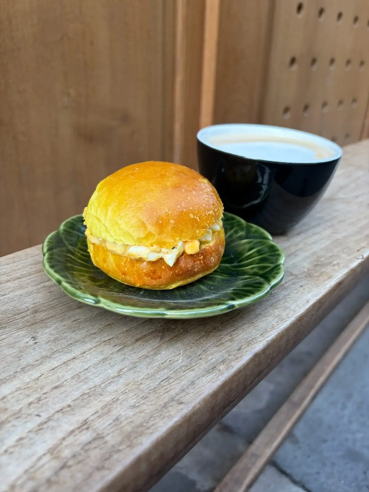 Un egg bun brioché et un café latte posés sur le rebord en bois de la devanture