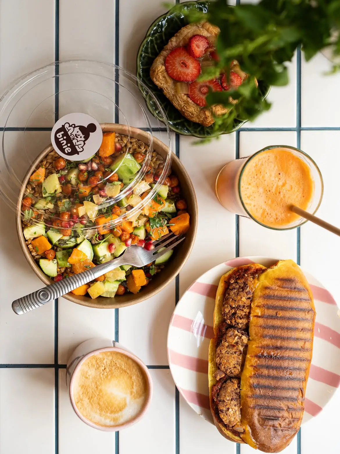 Une salade, un panini et un jus de carotte posés sur une table carrelée