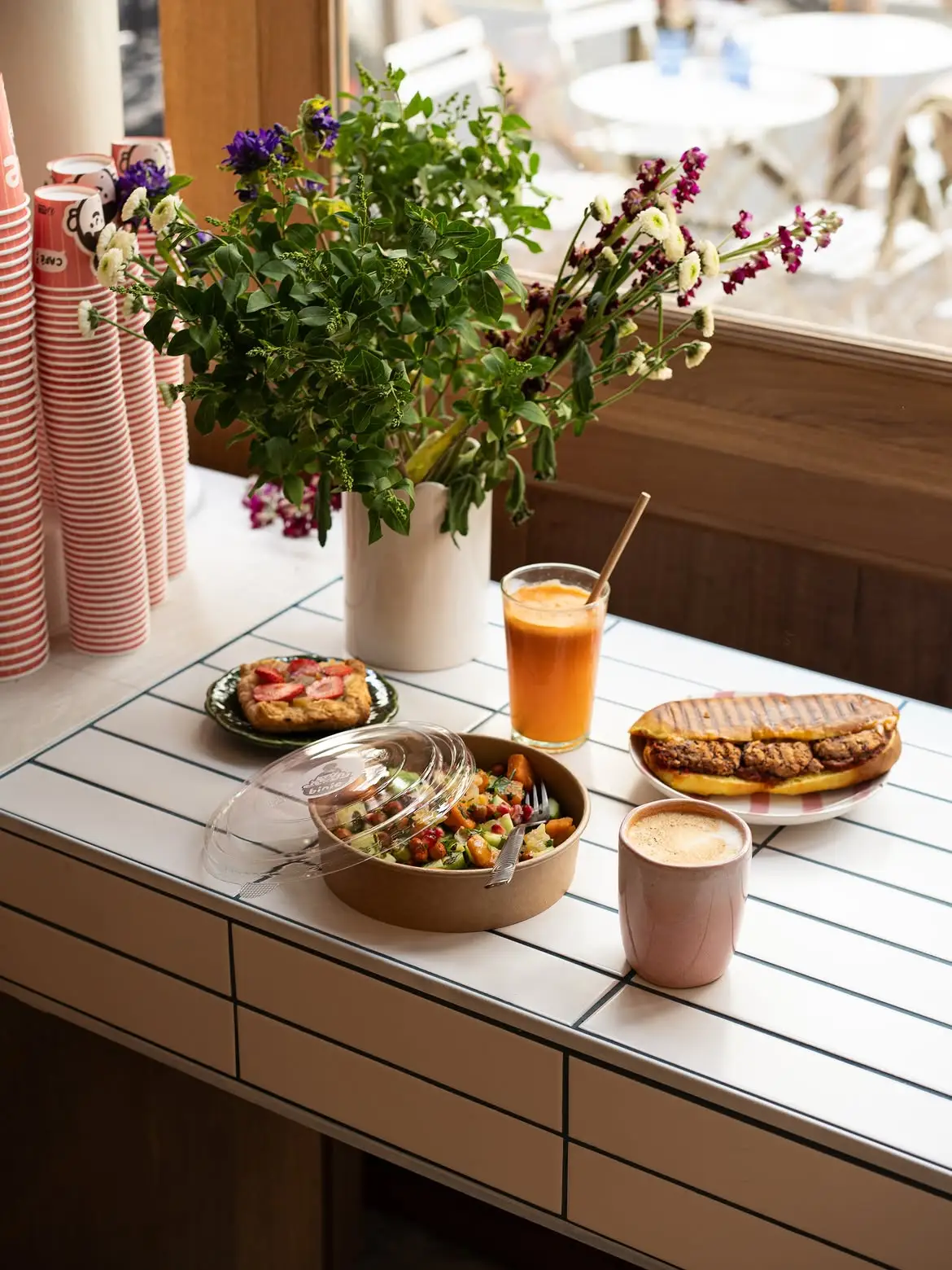 Table dressée avec une pile de gobelets Binie, un bouquet et une salade