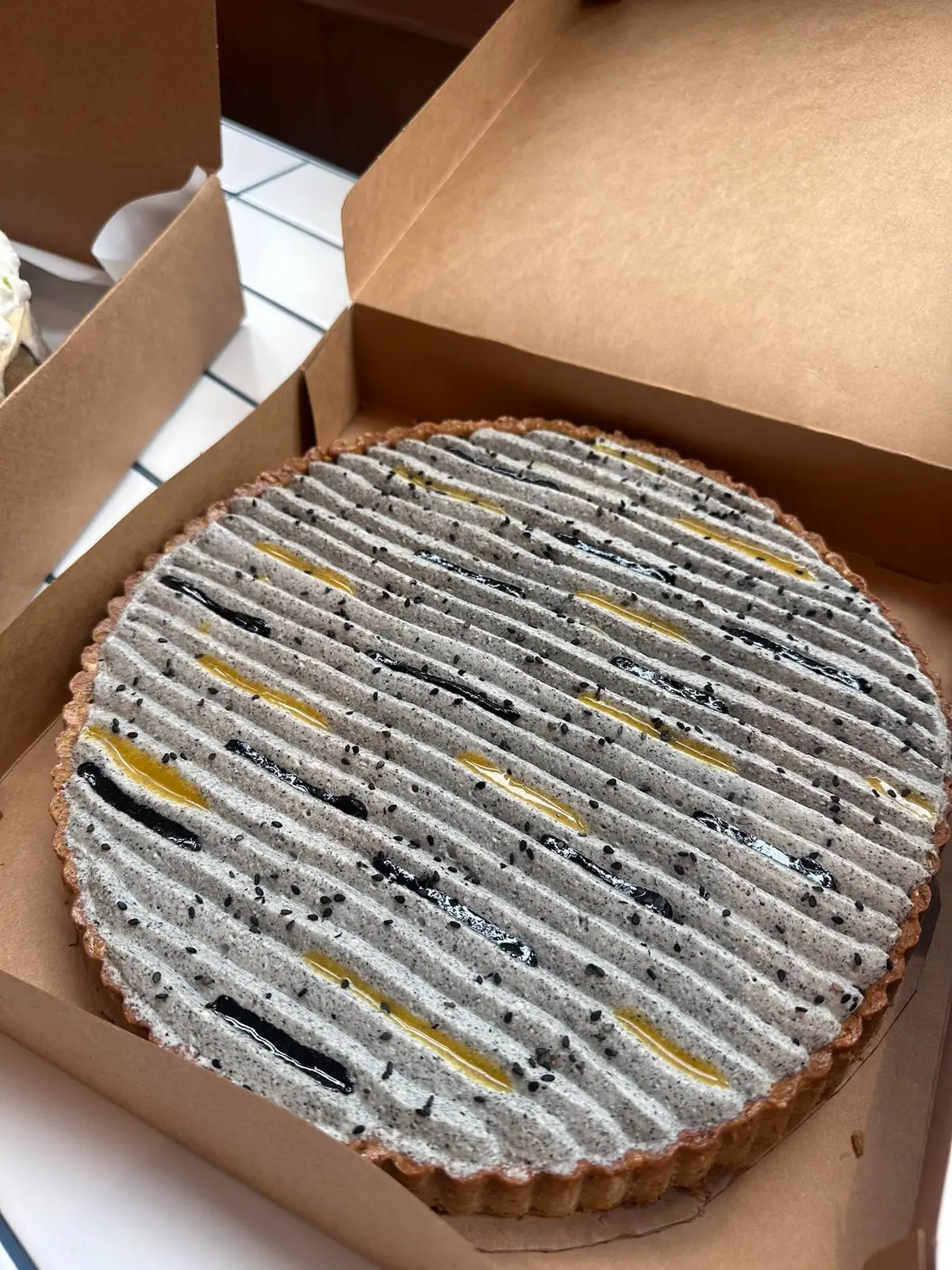 Grande tarte passion et sésame noir préparée par Binie, dans sa boîte de transport