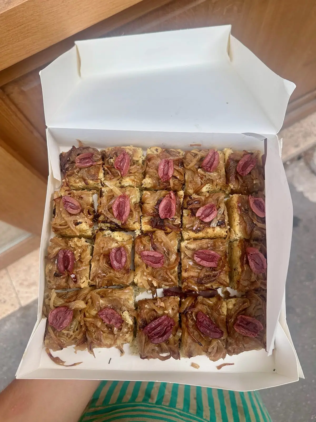 Pissaladière découpée en carrés, dressée dans sa boîte pour une livraison traiteur